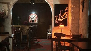 Een gedempt verlicht interieur met een stenen muur, een houten tafel en een rustieke sfeer.