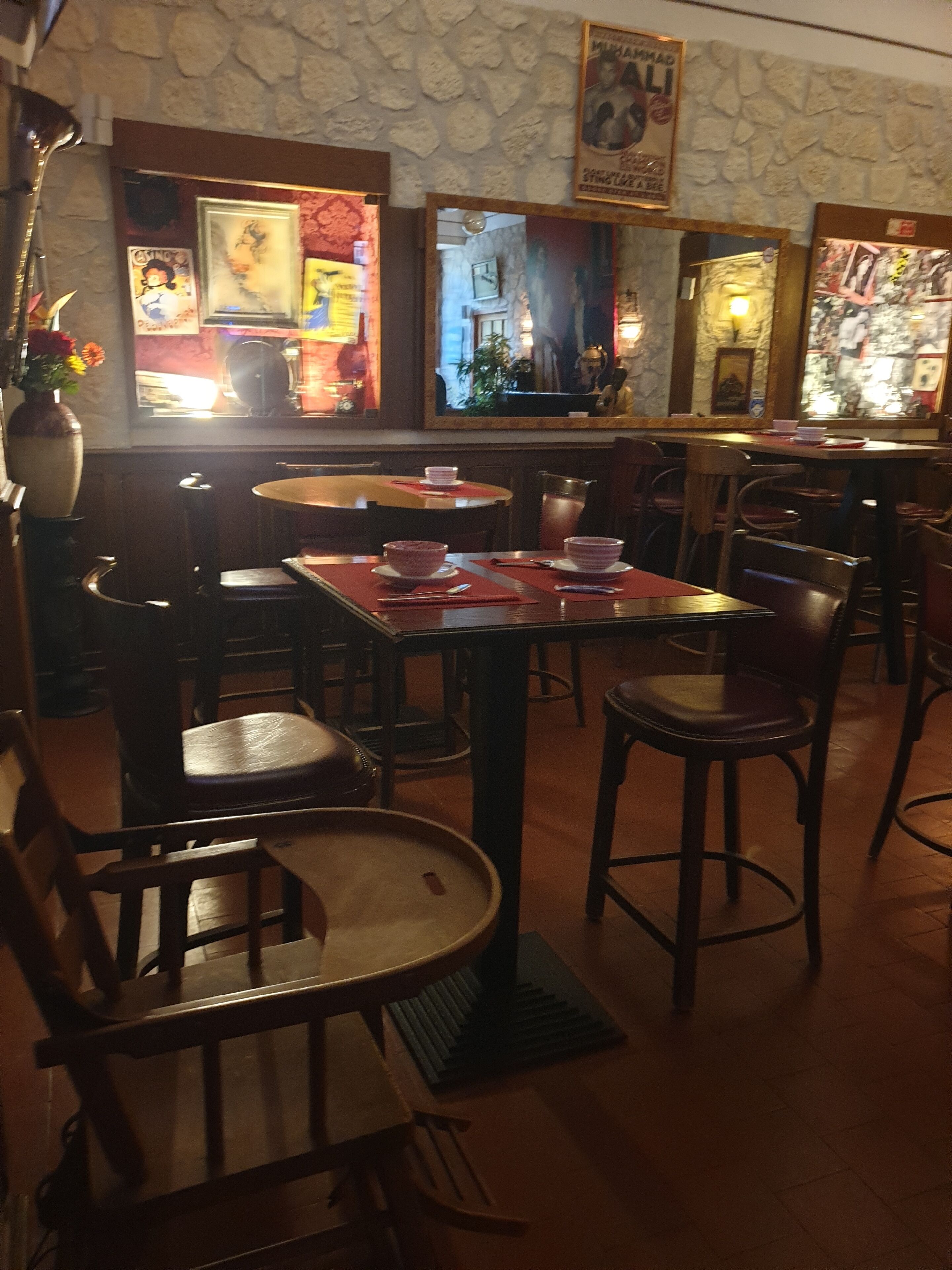 Ein Restaurantinneres mit Steinwänden, Holztischen und -stühlen sowie verschiedenen gerahmten Kunstwerken an den Wänden.