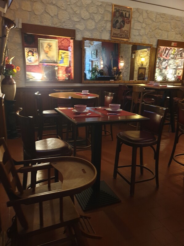 Un interior de restaurante con paredes de piedra, mesas y sillas de madera, y varias obras de arte enmarcadas en las paredes.