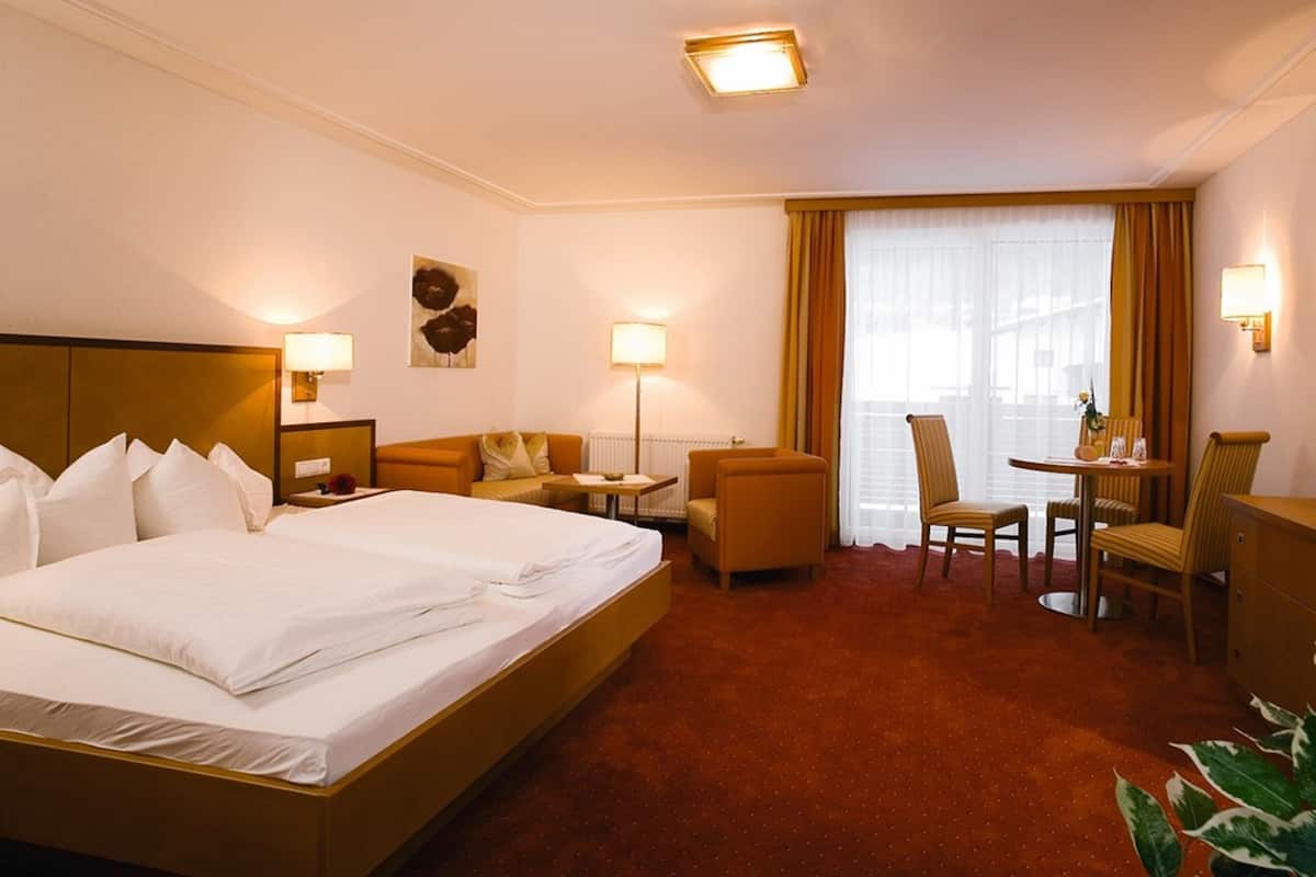 Quarto de hotel com uma cama grande, uma mesa, duas cadeiras e uma janela com cortinas.