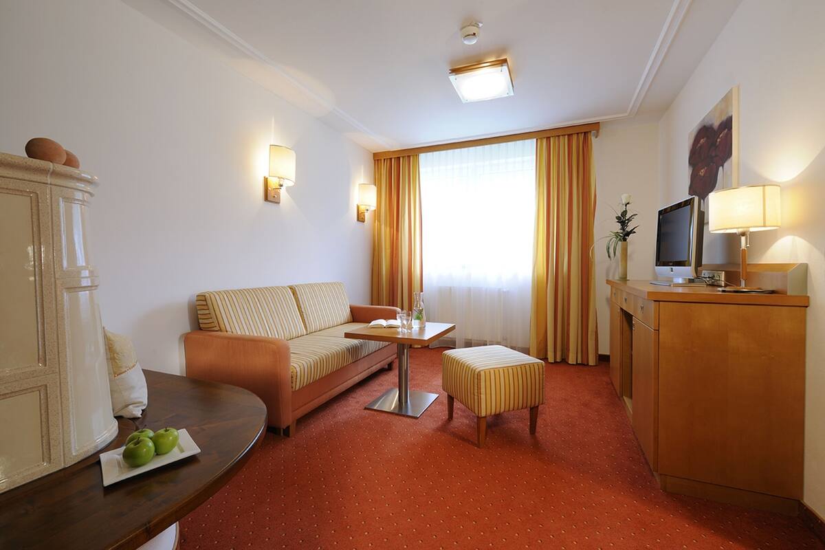 Quarto de hotel com sofá, mesa pequena, televisão e armário.