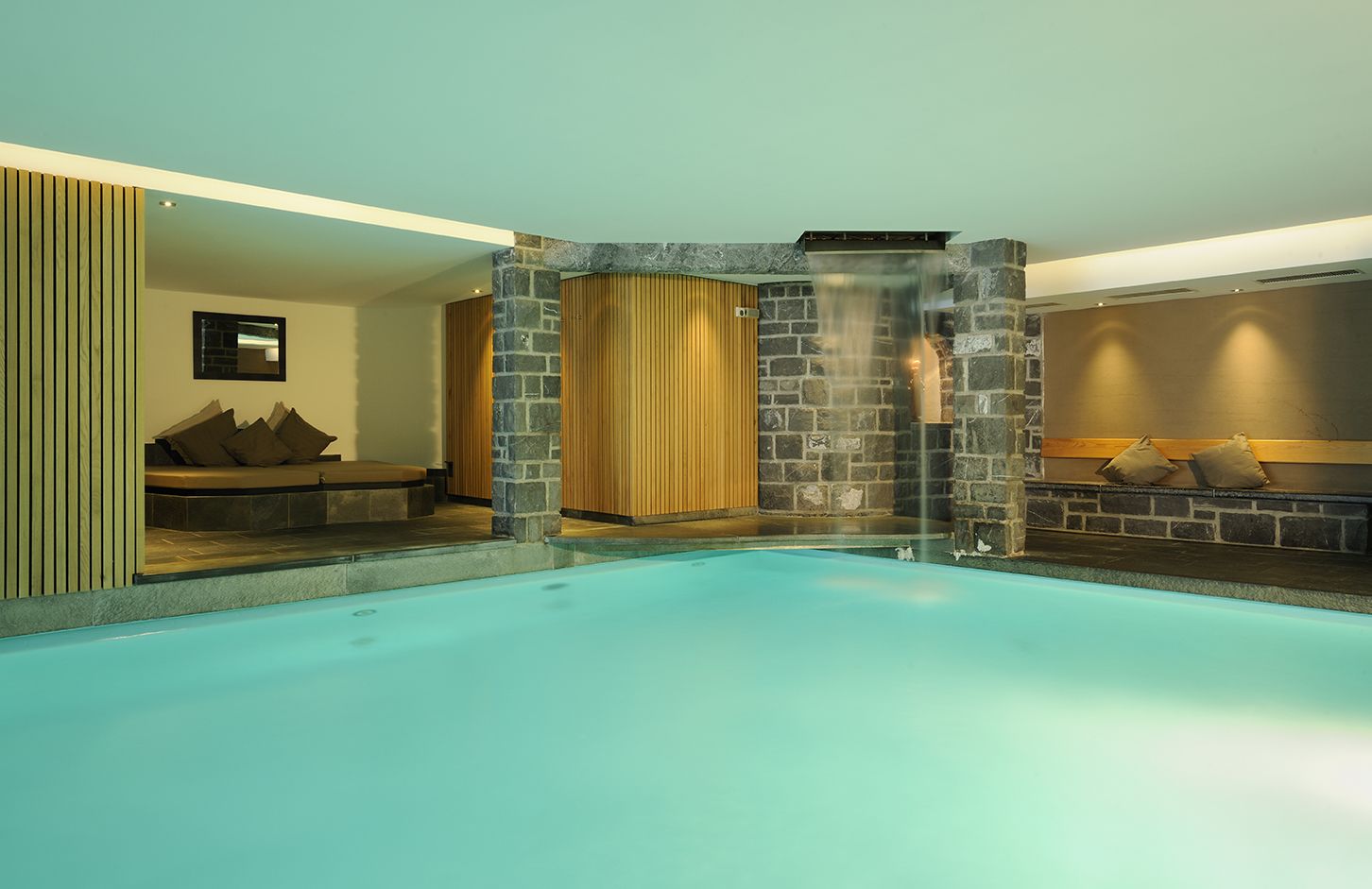 Une piscine avec un mur en pierre et un espace avec des bancs en bois.