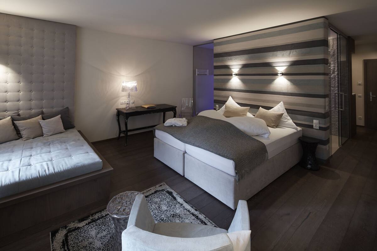 Quarto moderno com uma cama grande, um sofá menor, uma escrivaninha e uma parede listrada.