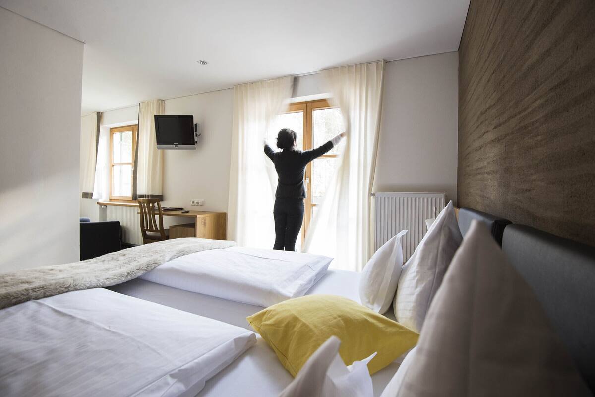 Quarto de hotel com duas camas, uma escrivaninha, uma cadeira, uma televisão e uma janela com cortinas.