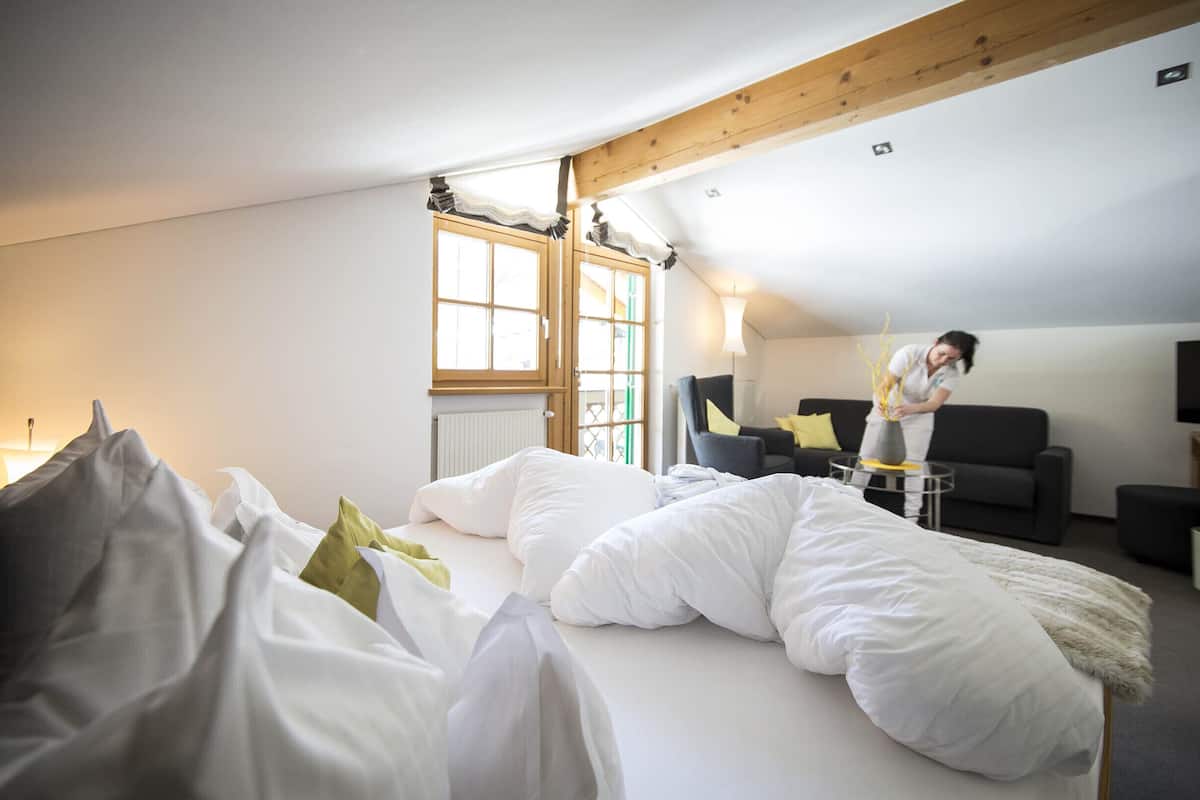 Quarto com cama, janela, luminária e uma pessoa perto da janela.