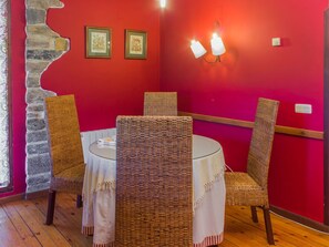 Un comedor con sillas de mimbre y una mesa redonda, paredes rojas y una pared decorativa de piedra.