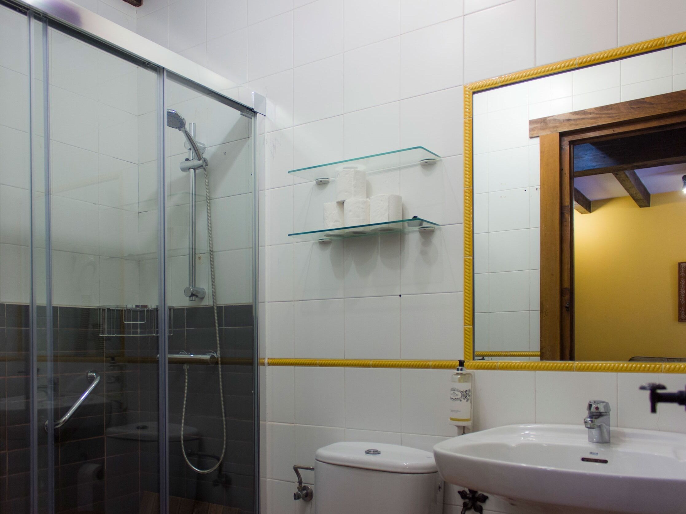 Un baño con cabina de ducha de vidrio, inodoro, lavamanos y espejo con marco amarillo.