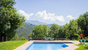 A rectangular swimming pool with a wooden deck and a view of mountains in the background. - Viviendas Rurales El Covaju (Cabezon de Liebana)