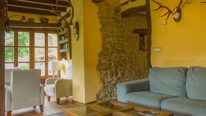 A cozy living room with a stone wall, a blue sofa, a wooden coffee table, and antler decorations. - Viviendas Rurales El Covaju (Cabezon de Liebana)