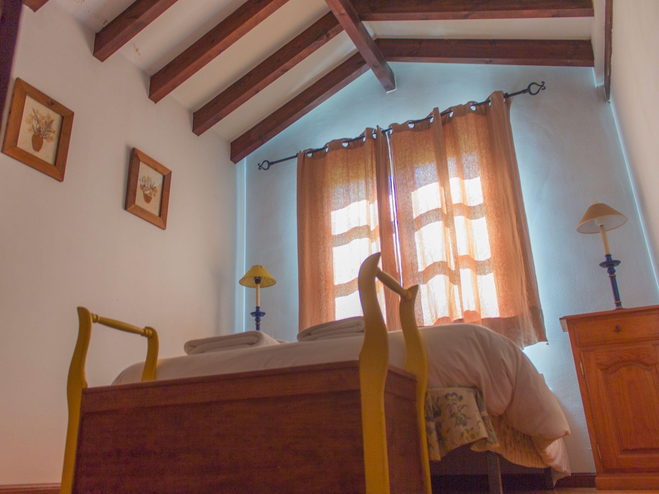 Een slaapkamer met een houten bed, een raam met gordijnen, een lamp en een dressoir.
