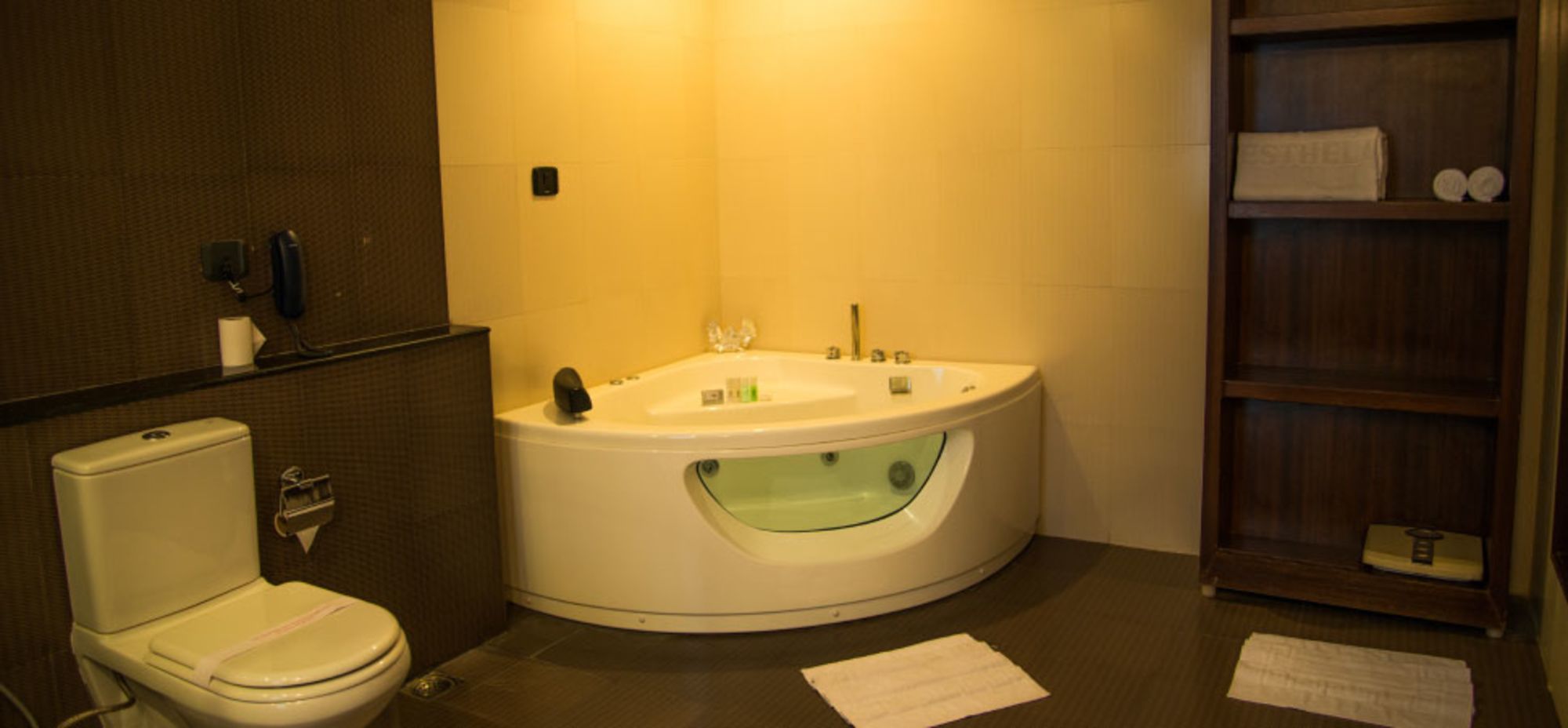 A bathroom with a toilet, a bathtub with a glass-enclosed shower, and a wooden shelf with toiletries.