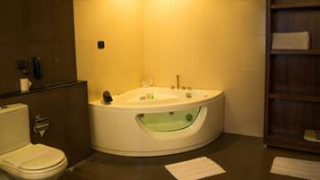 A bathroom with a toilet, a bathtub with a glass-enclosed shower, and a wooden shelf with toiletries.