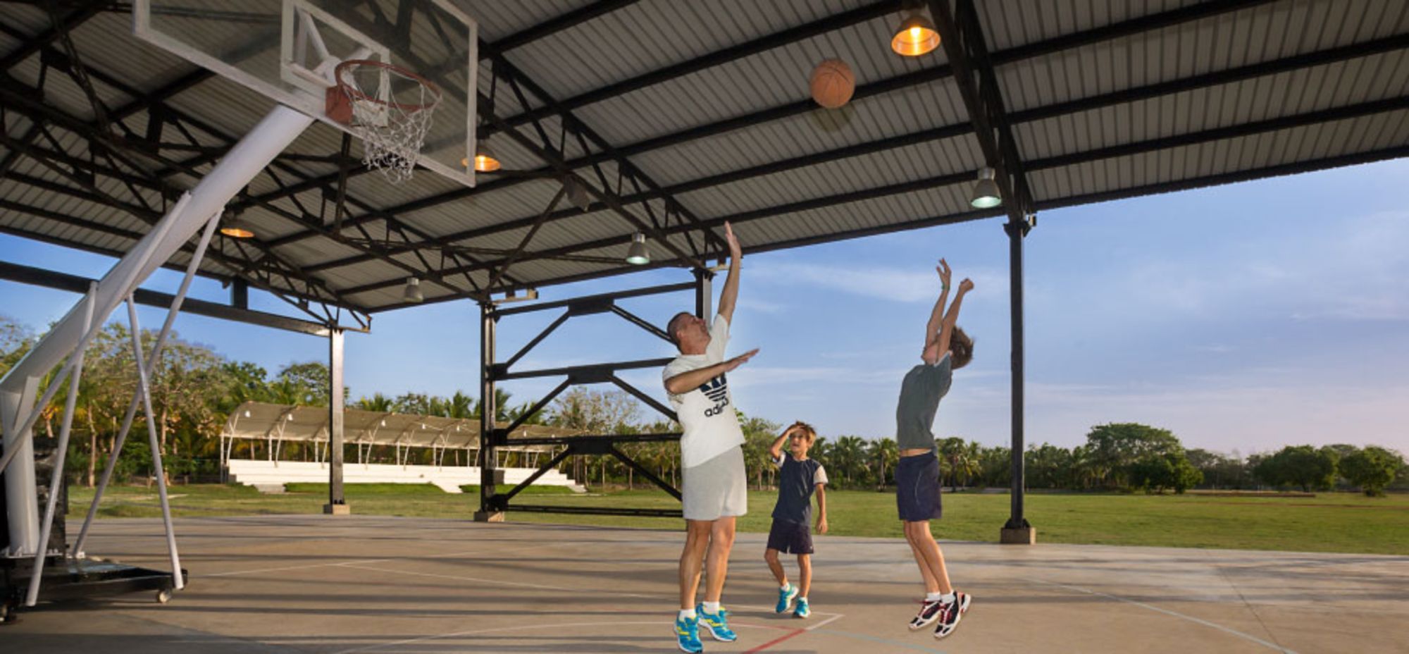 Una cancha de baloncesto al aire libre con estructura de techo metálico, aro y red.
