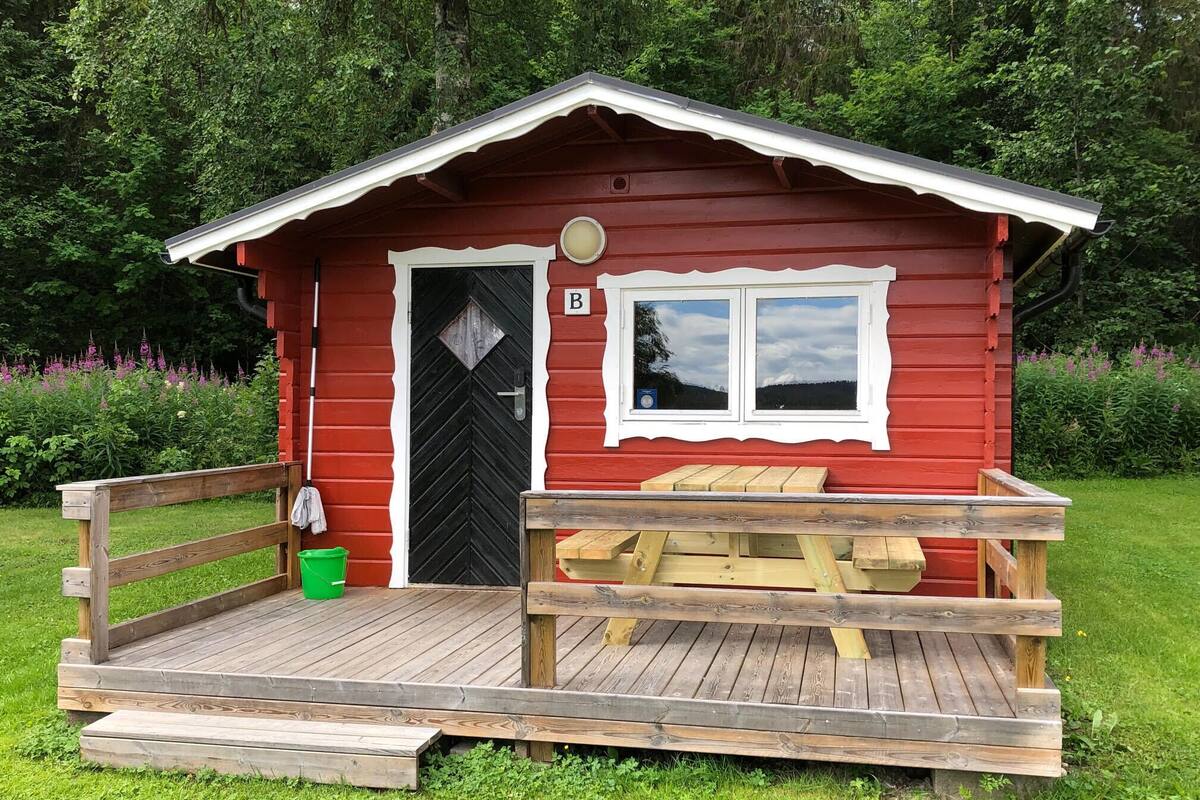 A red cabin with a black door, a small porch, and a picnic table.