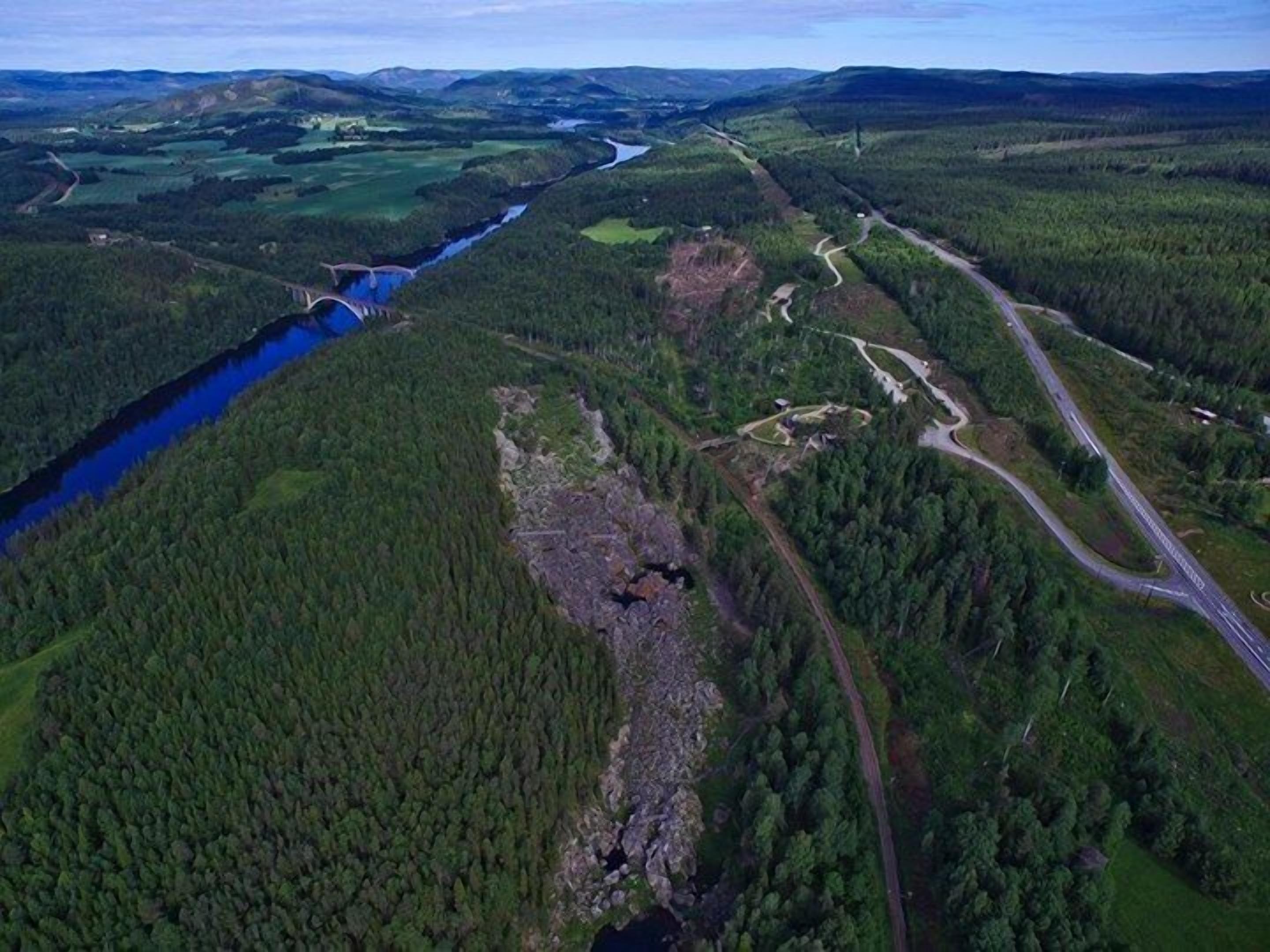 Une rivière traversée par un pont, entourée d’une forêt dense et bordée d’une route.