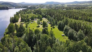Une vue aérienne d’une zone boisée avec un lac, un pont et plusieurs bâtiments qui semblent être utilisés à des fins d’hébergement ou de loisirs.