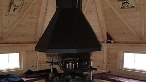 Une cabane en bois dotée d’un poêle en bois noir placé au centre, de murs en bois et d’un parquet disposé en motif à chevrons.