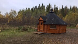Une petite cabane en rondins, dotée d’un toit à forte pente, d’une porte d’entrée et d’un petit porche.