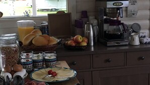 Une table de petit-déjeuner avec divers aliments, une machine à café et une vue sur l’extérieur.