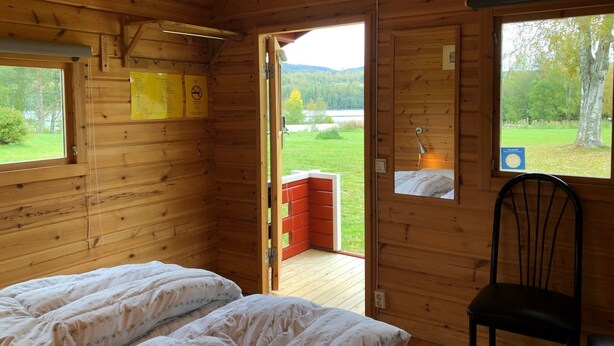 Une chambre dans un chalet en bois, avec deux lits, une chaise et une vue sur un lac et une forêt.