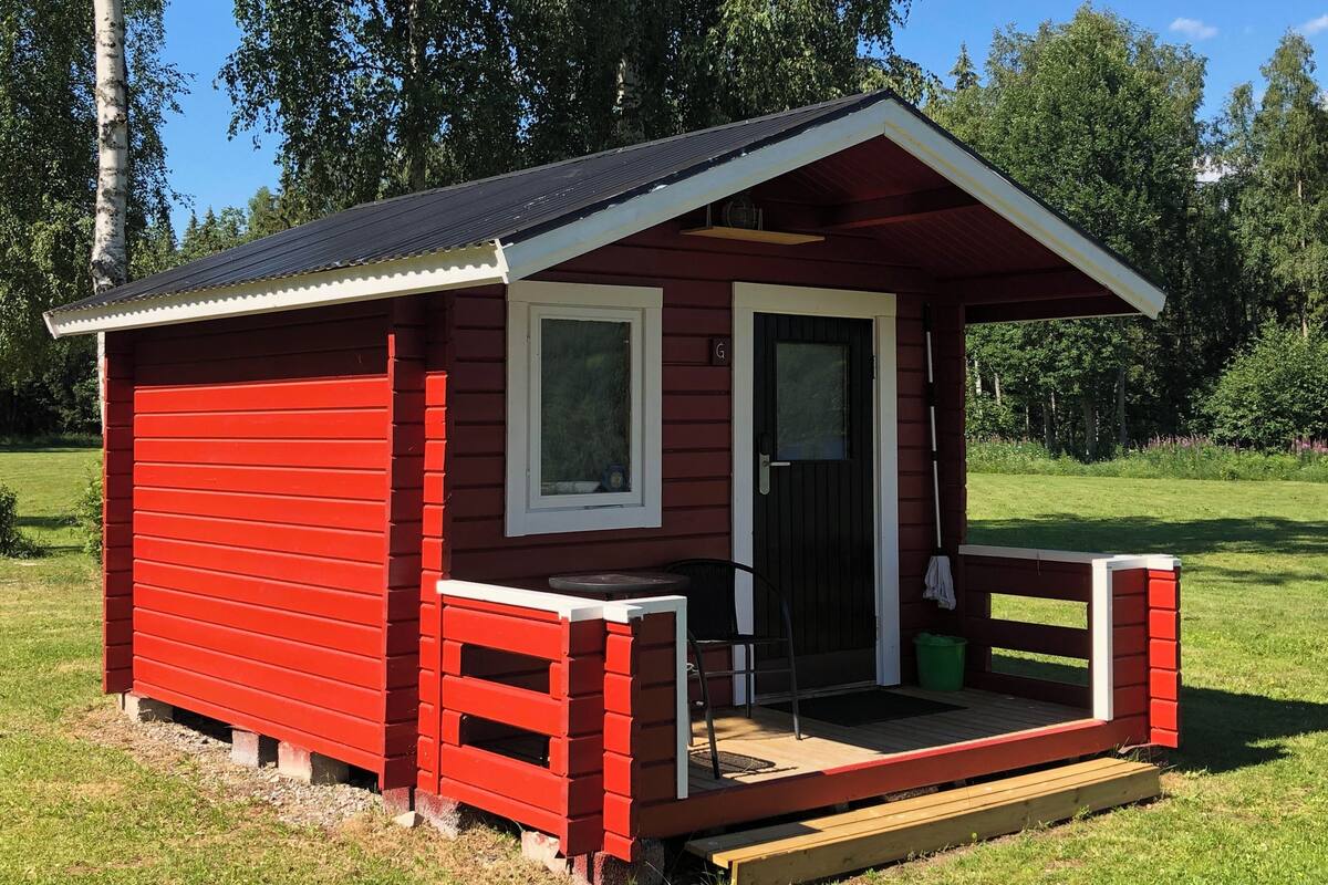 A small red cabin with a porch, a door, and a window.