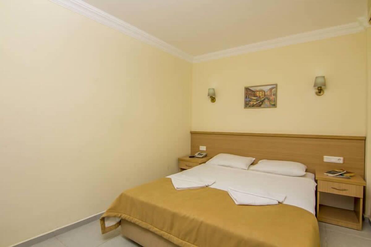 A hotel room with a single bed, two bedside tables, a nightstand, and a wall-mounted lamp.