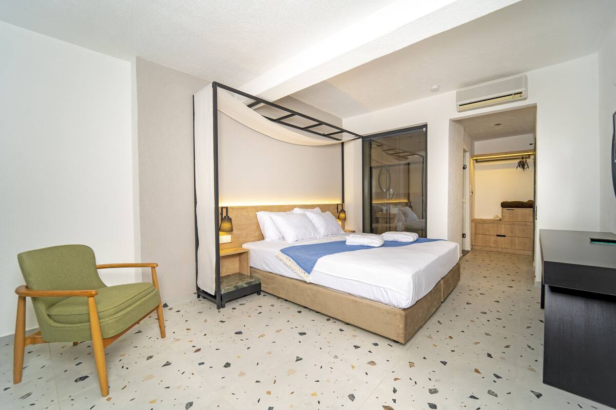 A modern hotel room with a large bed, a green chair, and a walk-in closet.