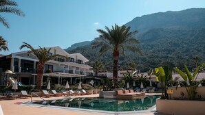 A pool area with lounge chairs and umbrellas, surrounded by palm trees and a mountain backdrop. - Hotel Karbelsun (Fethiye)