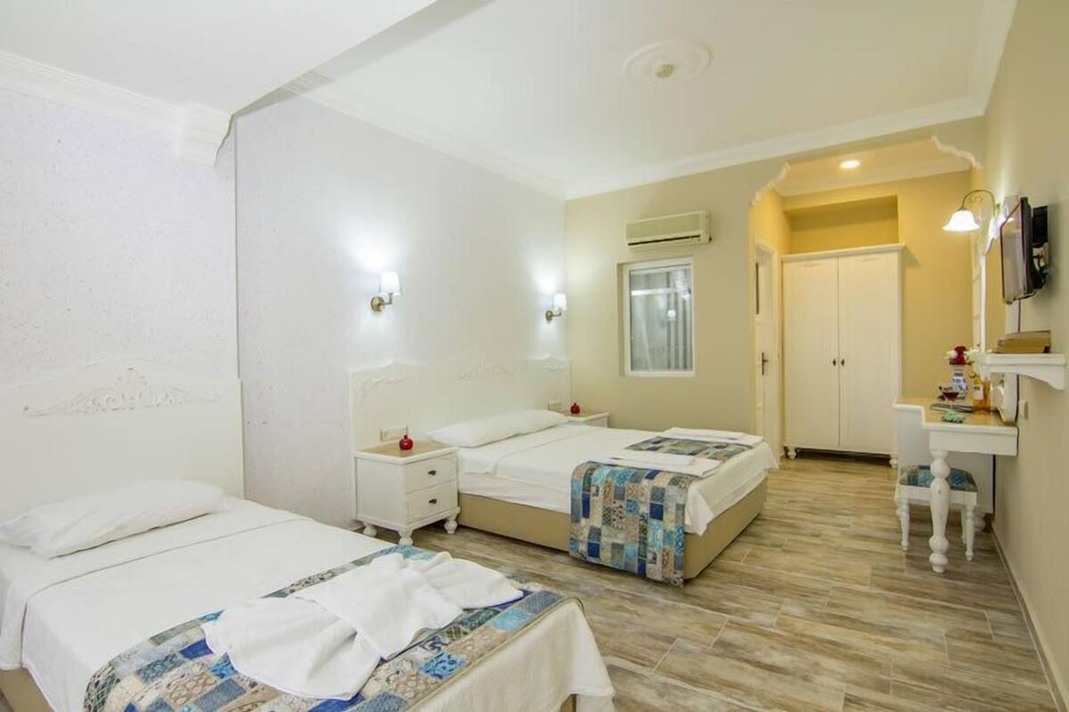 A hotel room with two beds, a small desk, a chair, a TV, and an air conditioning unit.