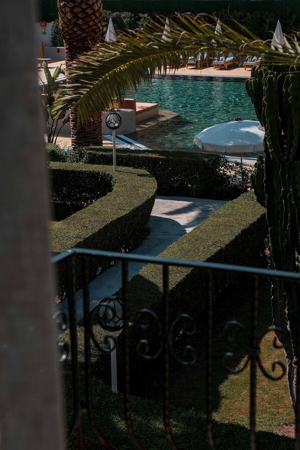 A pool area with neatly trimmed hedges, lounge chairs, and a palm tree.