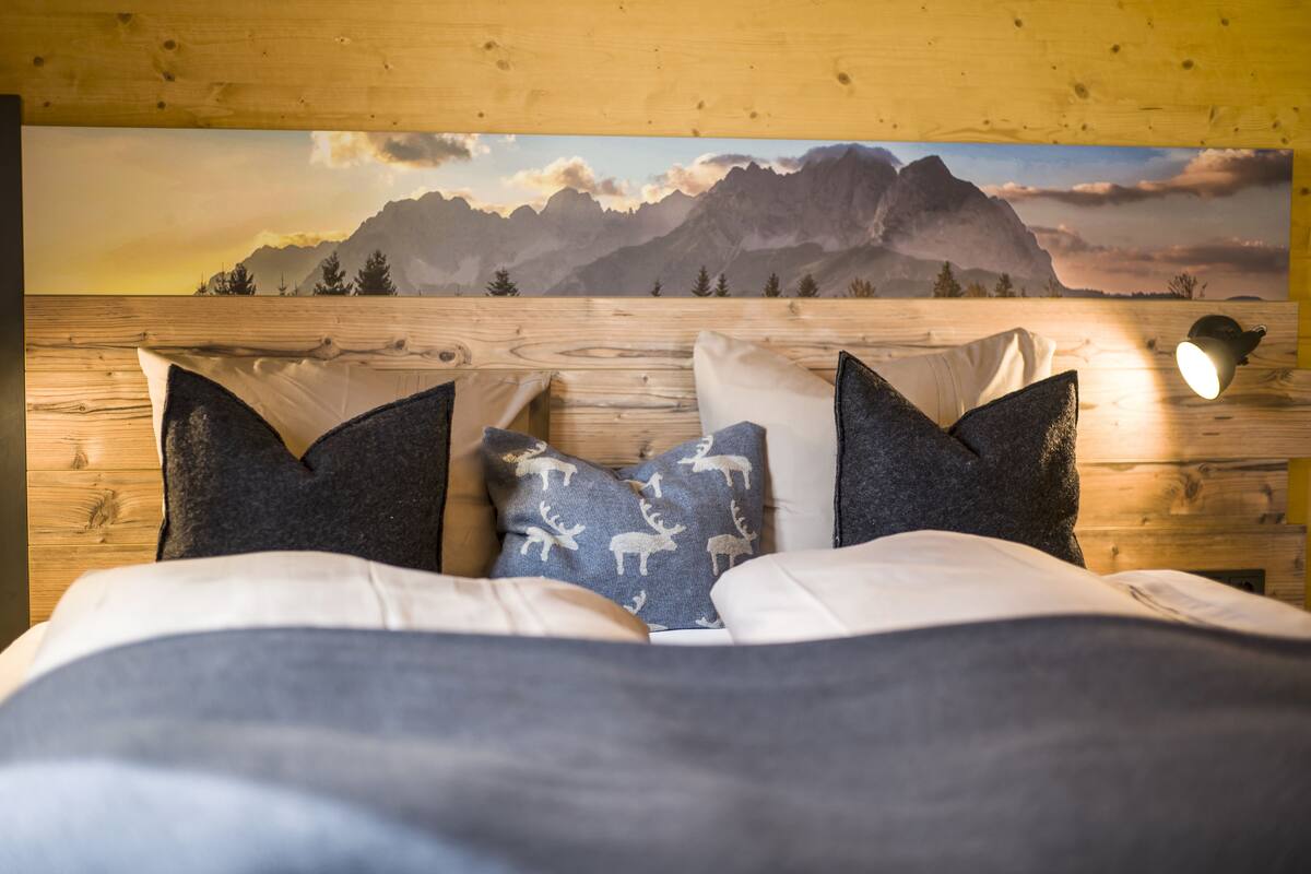 Un lit avec vue sur les montagnes en arrière-plan, une tête de lit en bois et deux oreillers.