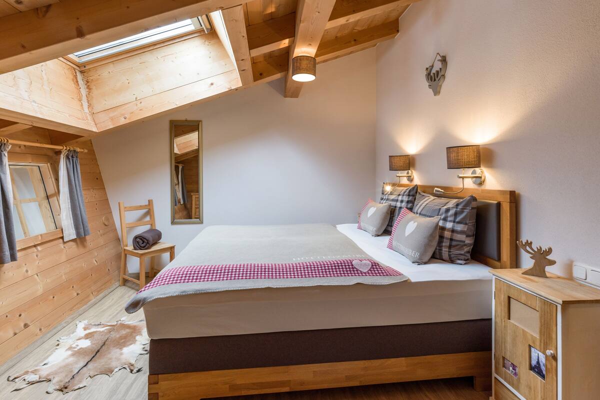 Une chambre avec un plafond en bois, un lit recouvert d’une couette à carreaux, un miroir et une armoire en bois.