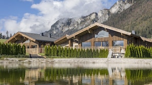 A wooden cabin with large windows and a reflection in the water, surrounded by trees and mountains. - Narzenhof Chalets - Familien & Luxus Apartments (Sankt Johann in Tirol)