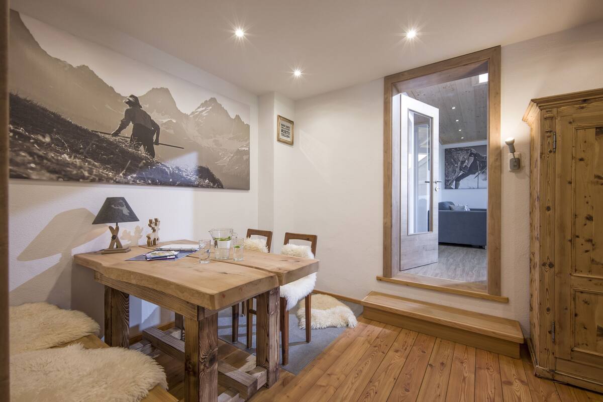 Un coin repas avec une table en bois, des chaises et un tableau représentant une montagne accroché au mur.