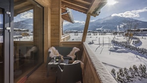 A wooden balcony with a table and chairs, overlooking a snowy landscape with mountains in the background. - Narzenhof Chalets - Familien & Luxus Apartments (Sankt Johann in Tirol)