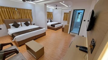 A modern hotel room with two beds, a desk, a chair, a small table, and a bathroom visible through an open door.