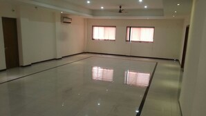 A spacious, well-lit room with a polished floor, two windows with curtains, and a ceiling fan. - Hotel Dhruv Palace (Trimbak)