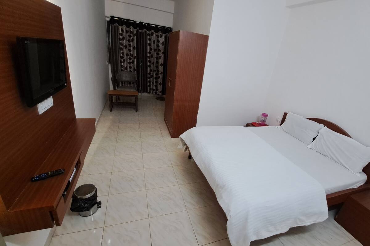 Ein Hotelzimmer mit Bett, einem an der Wand befestigten Fernseher, einem kleinen Tisch mit Fernbedienung und einem Papierkorb.