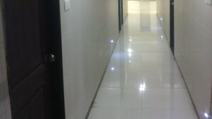 A long, narrow hallway with a shiny tiled floor and white walls. - Hotel Dhruv Palace (Trimbak)