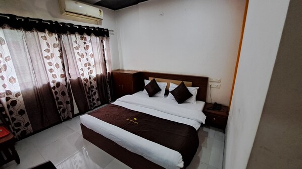 Habitación de hotel con cama, cortinas, mesita de noche con teléfono y unidad de aire acondicionado.