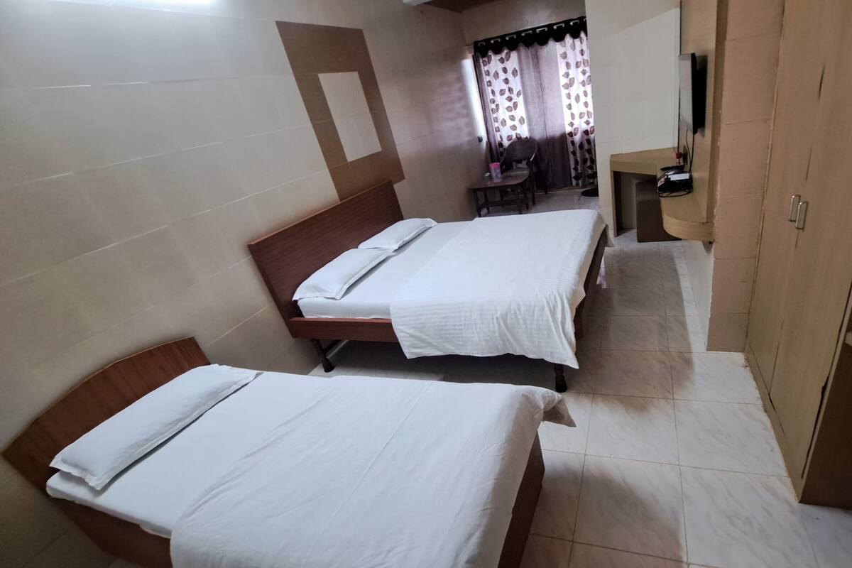Ein Hotelzimmer mit zwei Einzelbetten, einem kleinen Tisch, einem Stuhl, einem Fernseher und einem Kleiderschrank.