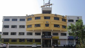 A multi-story hotel with a yellow and white facade, multiple air conditioning units, and a sign indicating it is a hotel. - Hotel Dhruv Palace (Trimbak)