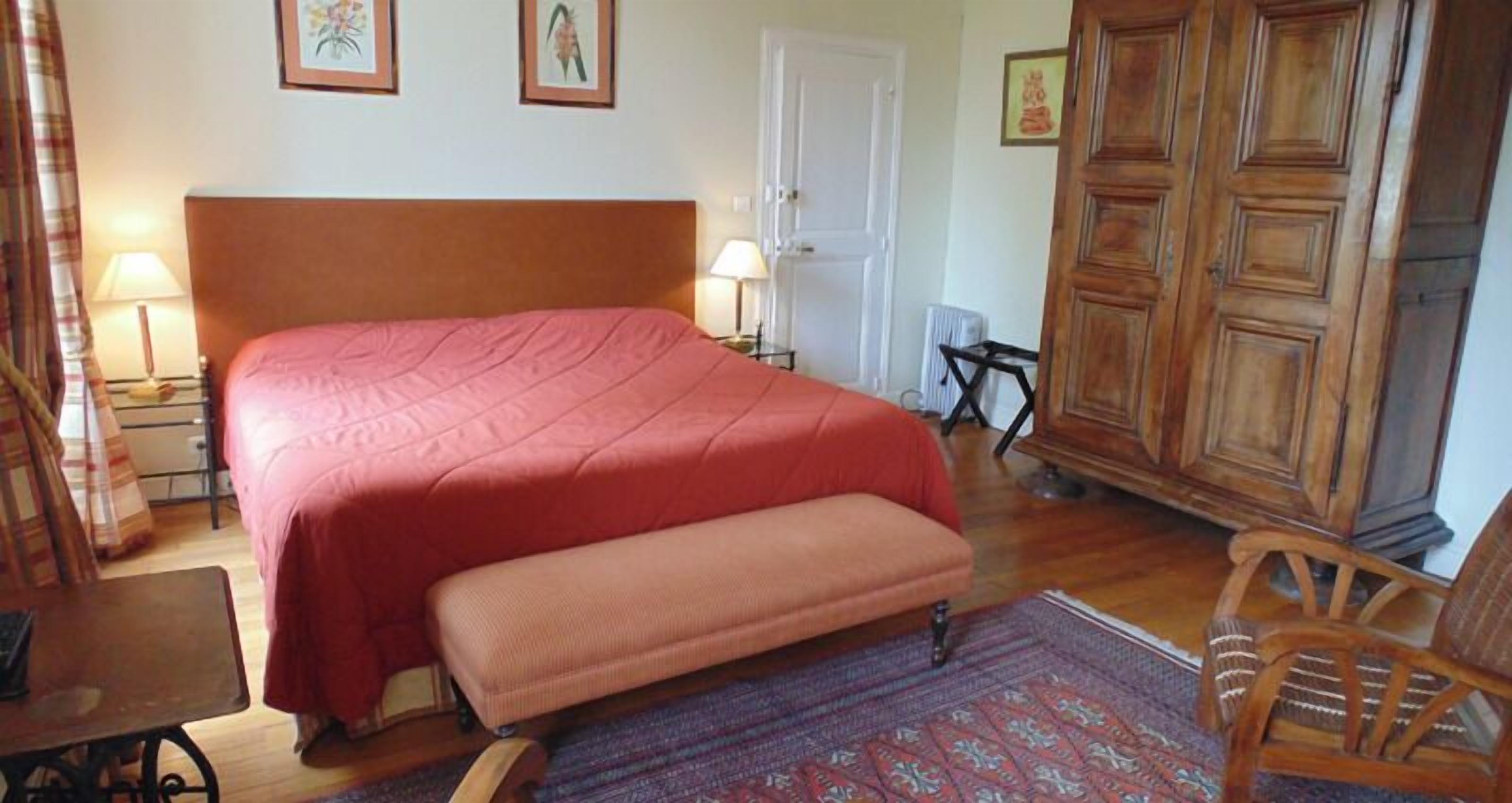 Une chambre à coucher avec un grand lit, une armoire en bois, un banc et une table.