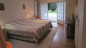 Ein Schlafzimmer mit einem großen Bett, einem Sessel, einer Lampe und Blick ins Freie durch eine Glastür.