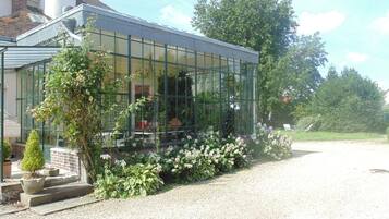 Une véranda dotée d’un toit en verre, entourée d’un chemin de gravier et agrémentée de diverses plantes.