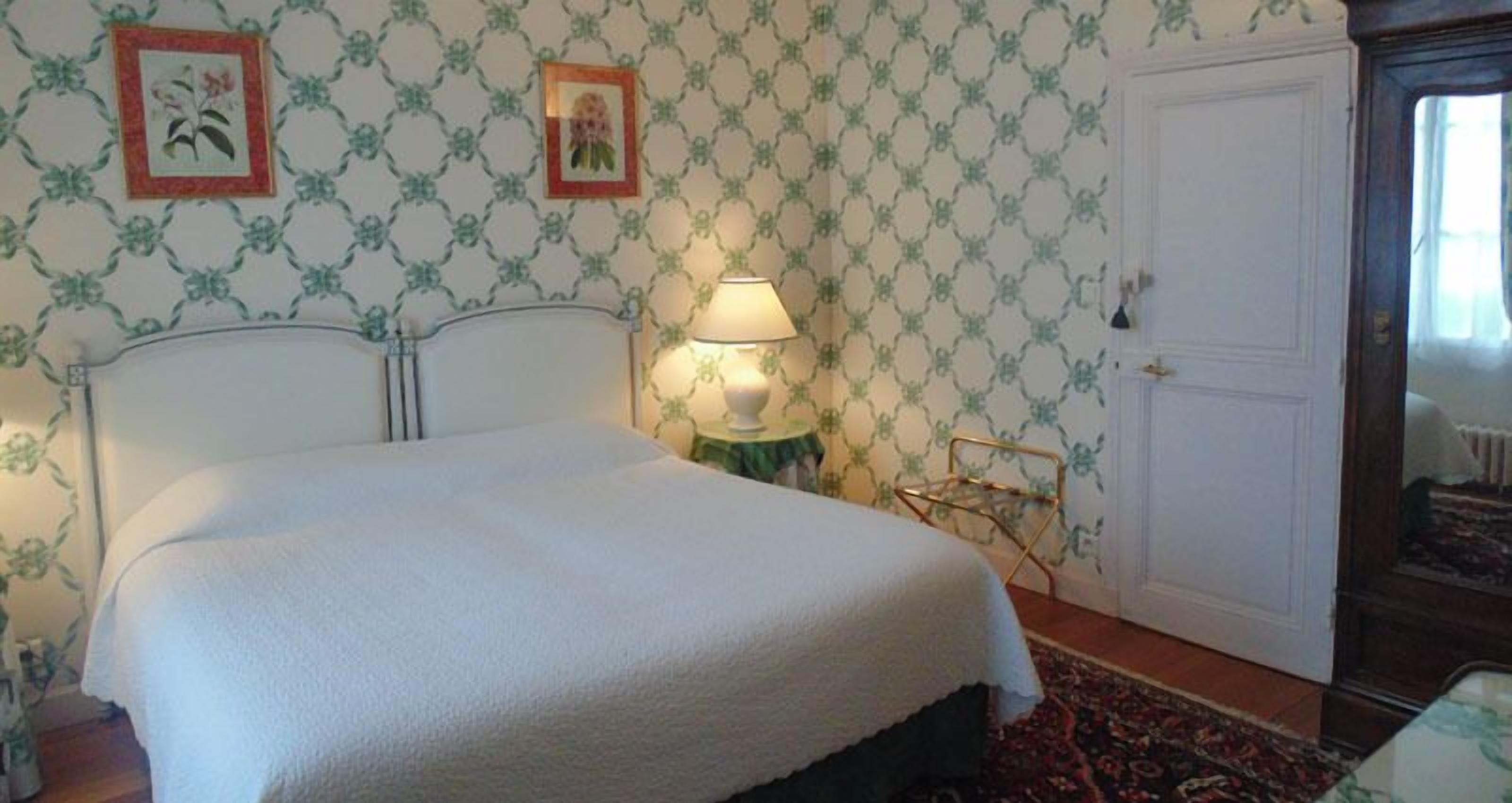 A bedroom with a bed, a bedside lamp, a door, and patterned wallpaper.