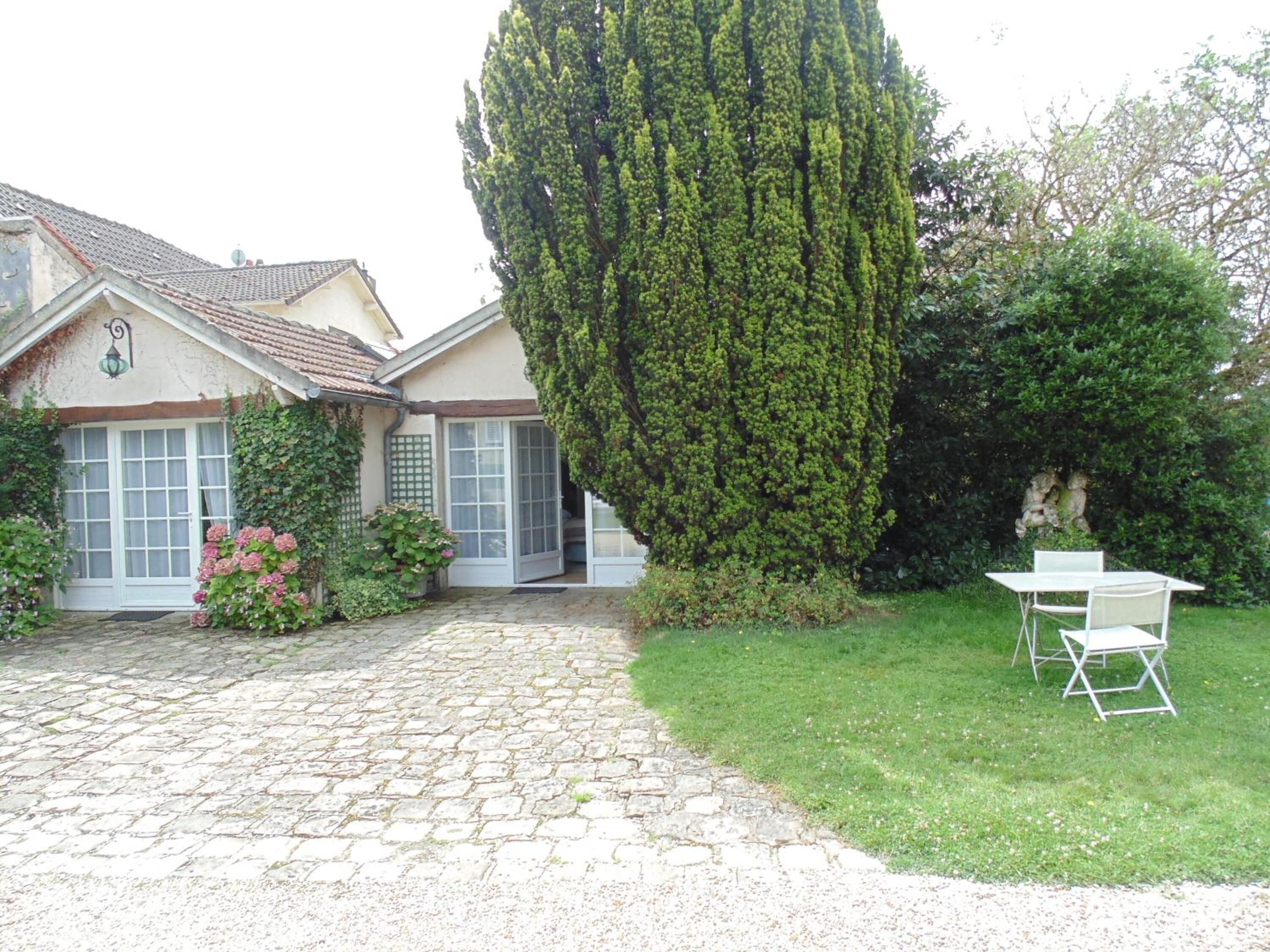 Una casa con un sendero de piedra que conduce a una puerta blanca, rodeada de follaje y un alto pino.