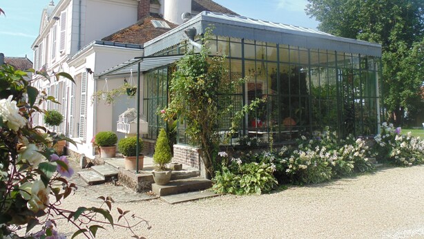 Ein Haus mit Wintergarten, Schornstein und einem Garten mit Blumentöpfen und Blumen.