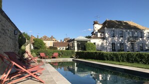 Ein Swimmingpool mit roten Liegestühlen, ein weißes Gebäude mit einem Turm und ein klarer, blauer Himmel.