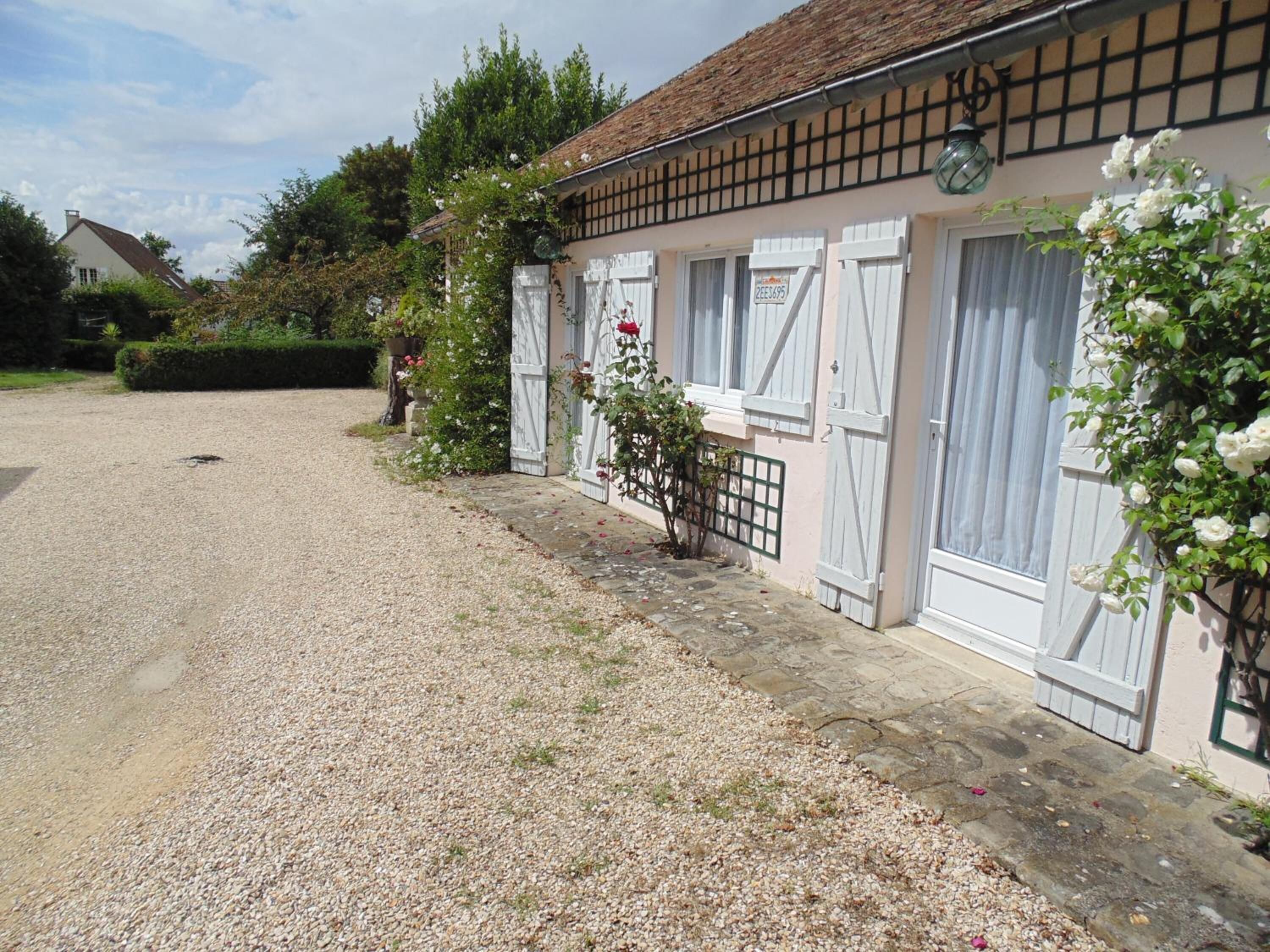 A building with a gravel driveway, white shutters, and a garden with white flowers.